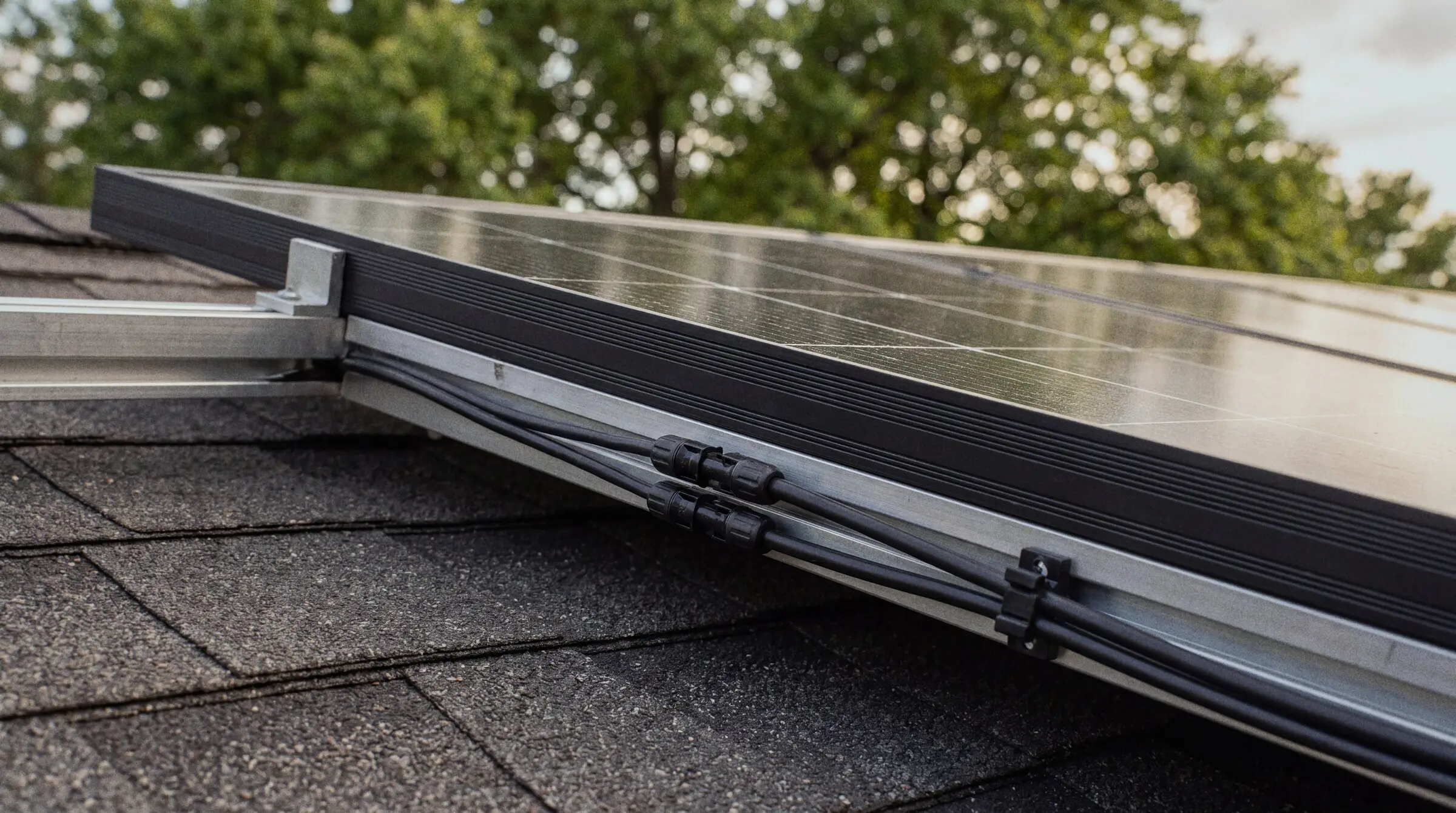 Solar cables and connectors clipped along the mounting rail at the edge of a rooftop panel